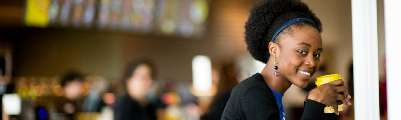 Female student smiling at camera with a yellow cup of coffee in her hands.